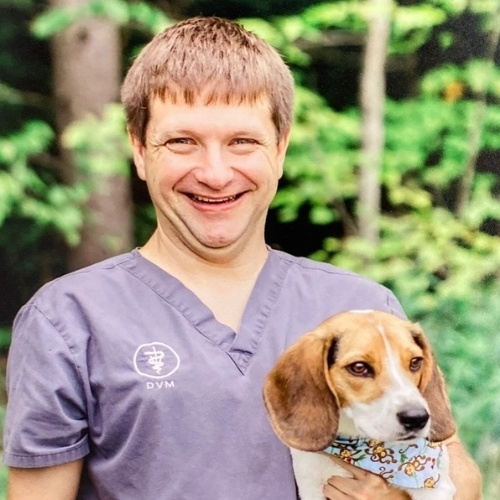 Dr Scott Adams holds a beagle puppy wearing a bandana.