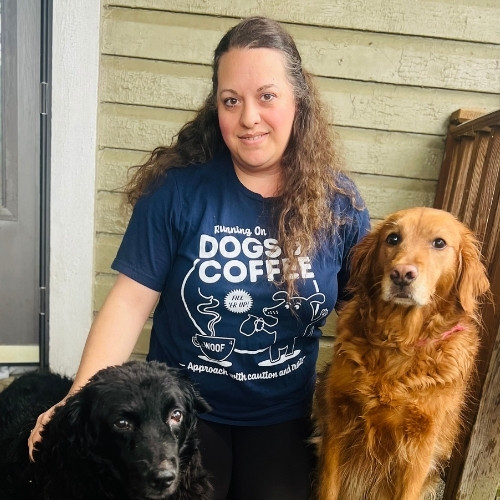 Andrea Philips wearing a dark blue t-shirt posing with a black dog and a golden retriever.